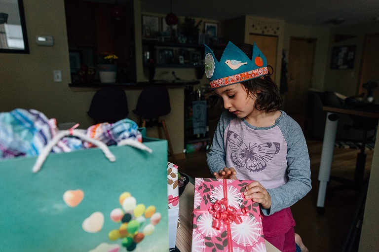 Girl wears crown while opening pink wrapped birthday gifts