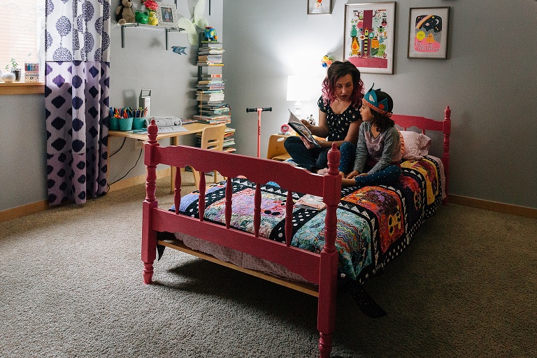 mom and daughter sit in a bright, colorful bedroom reading a book
