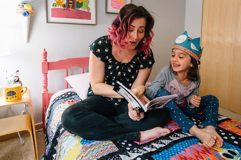 mom and daughter sit on colorful bed while reading a book with a lot of expression