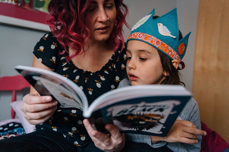 mom and daughter read a chapter book. daughter is wearing a birthday crown
