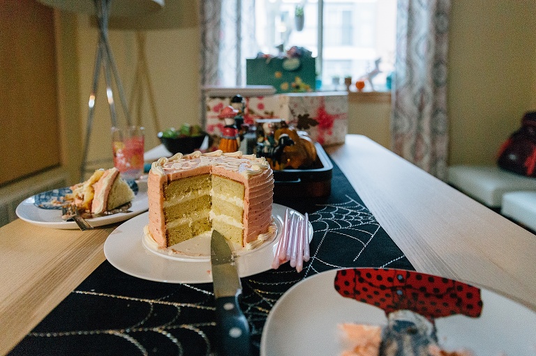 a pink layer cake with two pieces cut out sits on a table with a spider web runner