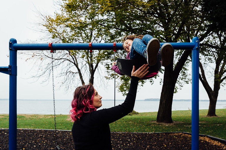 mom pushes girl on a swing with foggy lake in the background 