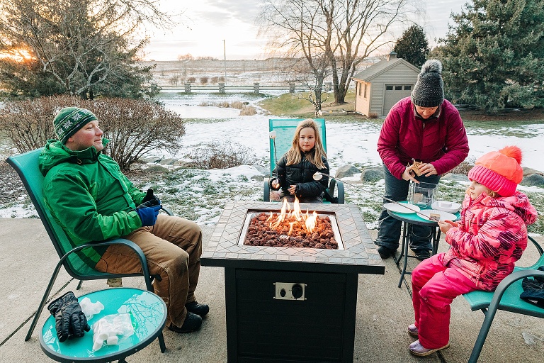 Family of four roasts marshmallows over a fire at sunset in the winter 