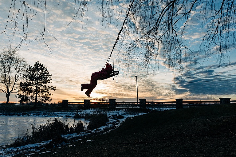 Girl swings on a swing above the horizon as a silhouette 