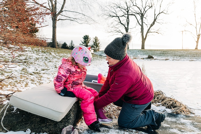 Mom helps daughter out of her ice skates and into boots after skating in winter 