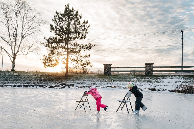 Girls use folding chairs on the frozen pond to stabilize them while ice skating 