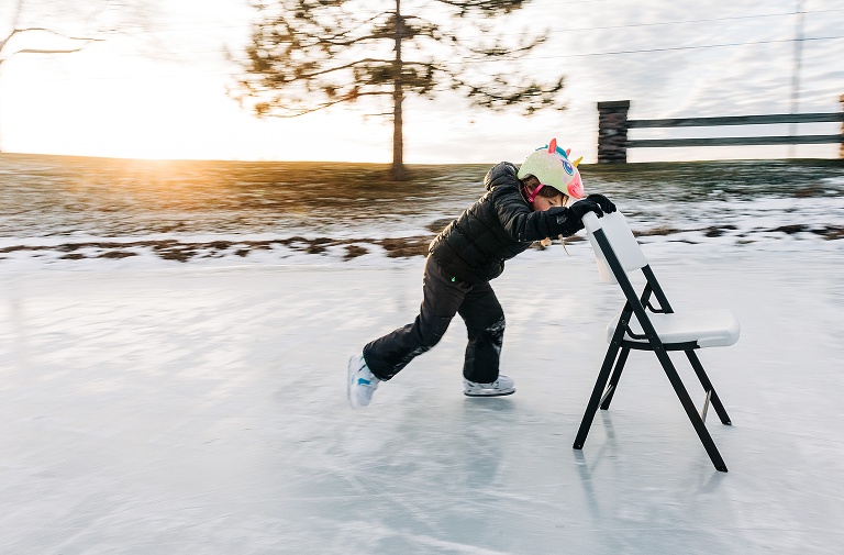 Girl ice skates holding onto a folding chair at sunset. Image shows motion blur