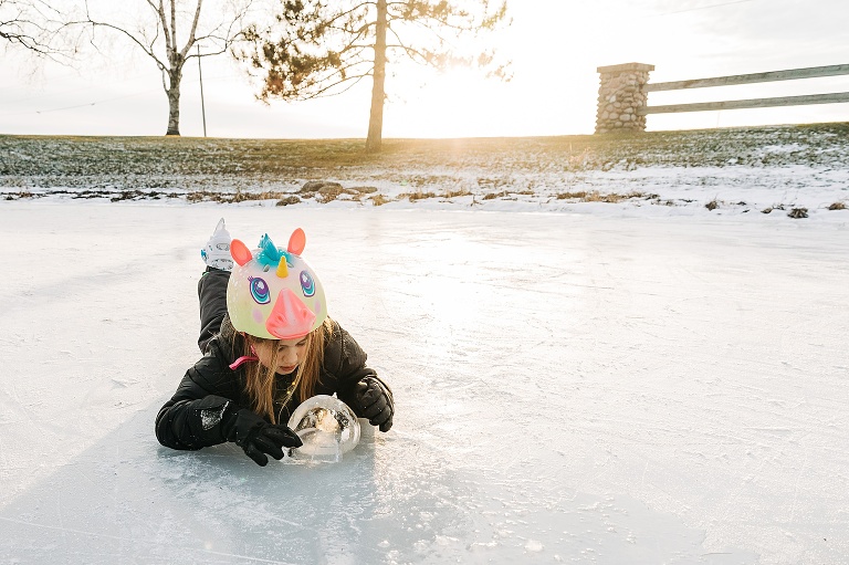 girl examines a ball of ice on the frozen pond, she lays on her belly and ice skates are in the air