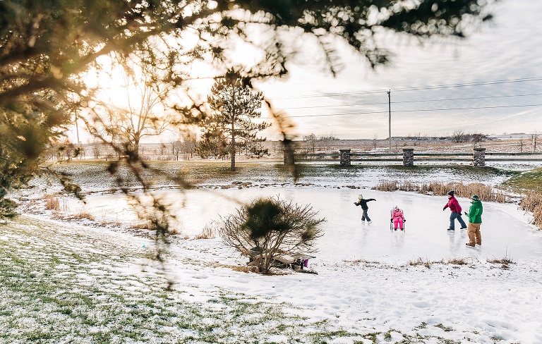 pulled back view of family of four ice skating on a pond at sunset 