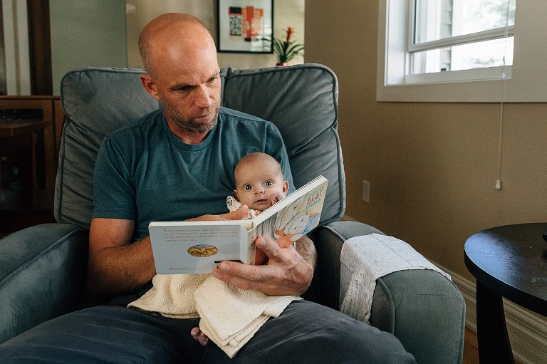 Baby sits on father's lap while he reads a children's board book 