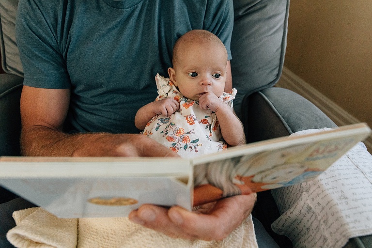 Baby sits on father's lap while he reads a children's board book 