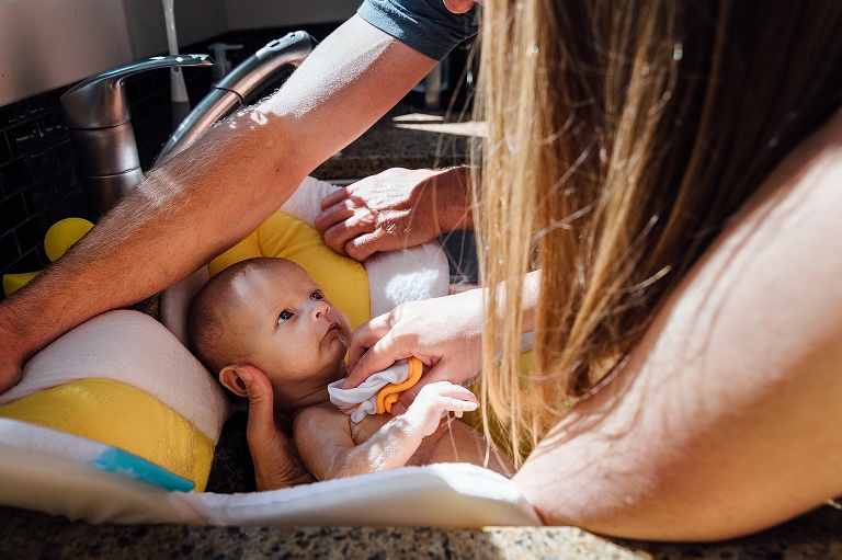 Baby in a sink bath has both parents supporting and washing 