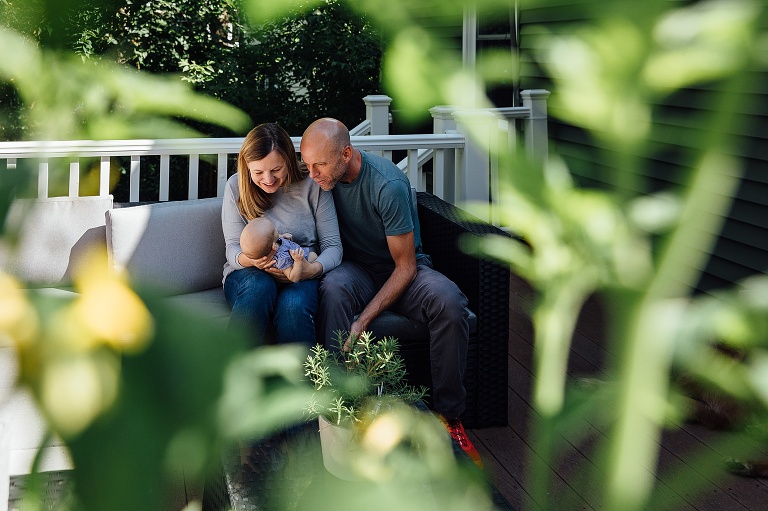 tomato plants frame parents holding and smiling at baby on a deck