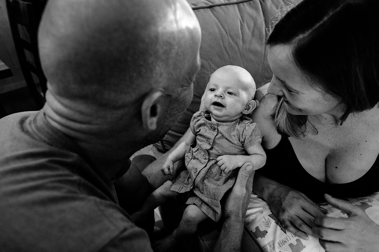 Baby smiles at dad; mom and dad frame baby. black and white