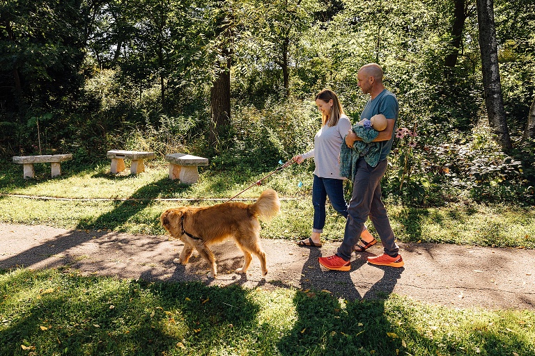 family of three takes golden retriever for a walk in the park 