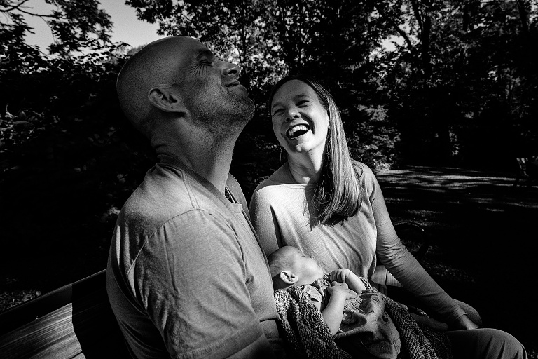 parents share a moment of laughter while newborn sleeps in father's arms 