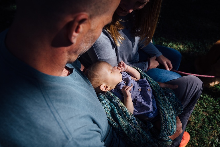 focus on baby sleeping in the sun and being held by parents on a bench