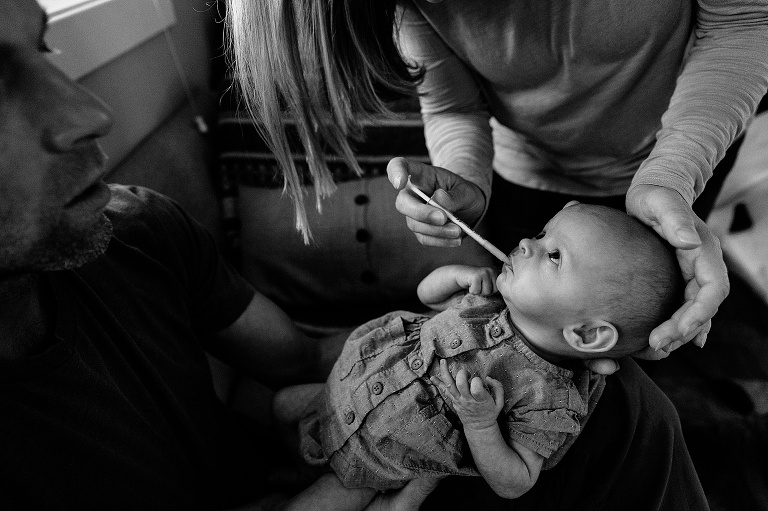 baby receives medicine and looks up at mother while father holds; black and white 