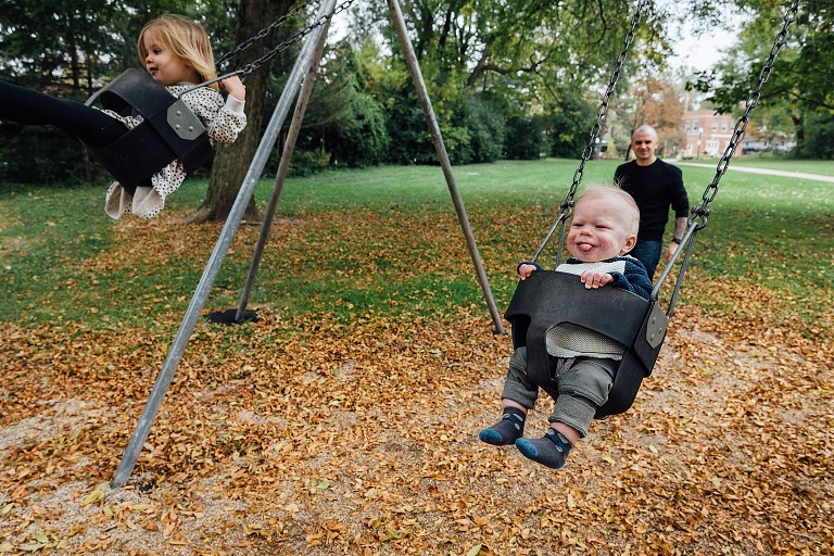 A preschool girl and toddler boy swing at the park on a foggy fall weekend