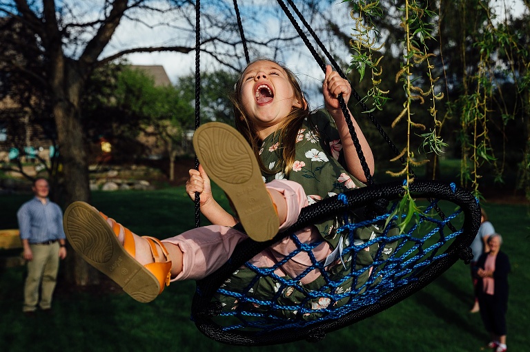 young girl on a hammock swings swings into a spring willow tree while family stands off to the side and cheers