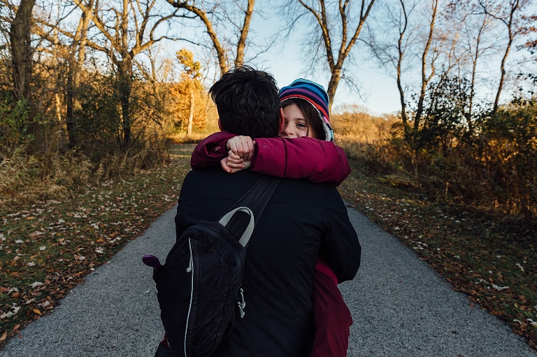 girl makes eye contact with camera while held by mother walking on an autumn path
