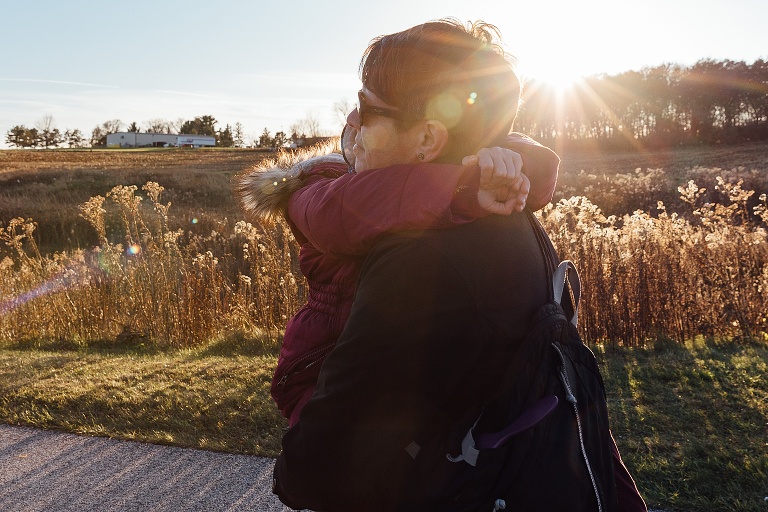 mom carries young girl on an autumn path with sun flare on the horizon
