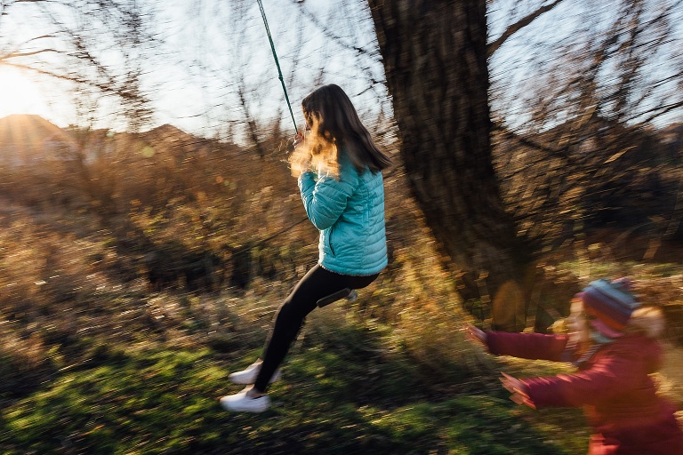 panning movement of girl on swing and younger sisters pushing her; sun in the background 