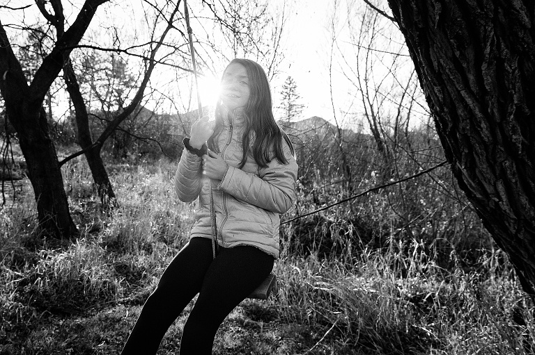 black and white; preteen on a wooden bench swing with sun flare in the background 