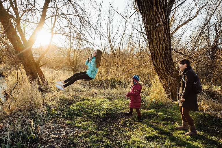 sisters swing on a wooden bench swing with sun flare on the background 