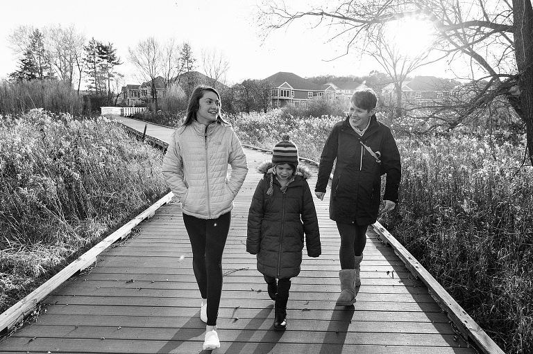 sisters and their mother walk on a boardwalk on a cold autumn day