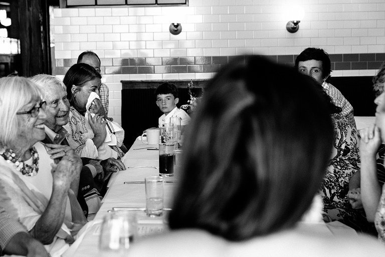 Woman dabs teary eyes with a white napkin at the end of a long table during an 80th birthday celebration