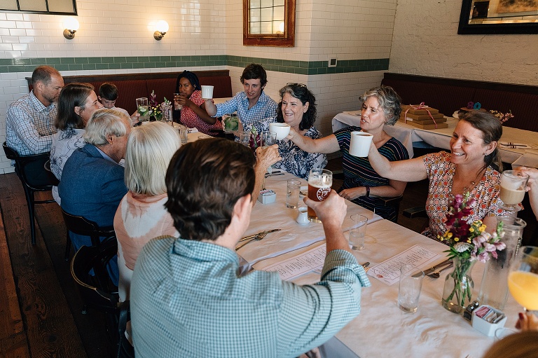  people at a long restaurant table making a "cheers" gesture with their cups for an 80th birthday celebration
