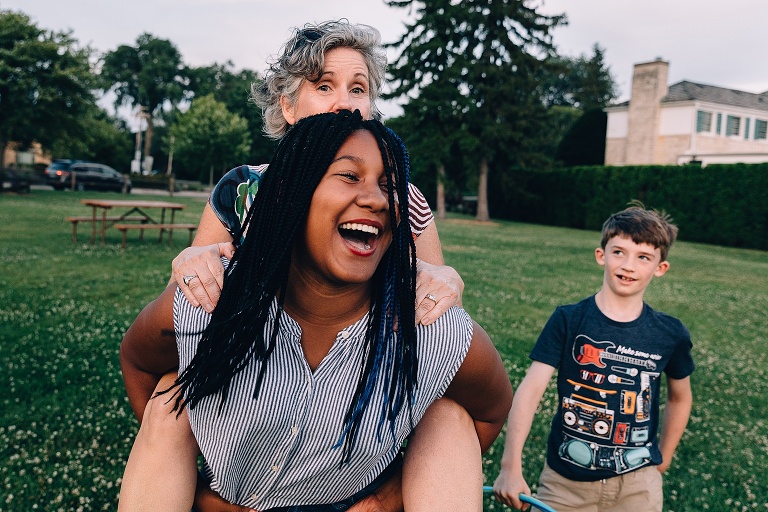 teen girl with mother on her back for a piggy back ride smiles huge while younger brother looks on, smiling 