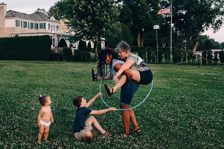 teen daughter give her mother a piggy back ride while son puts a hula hoop over them