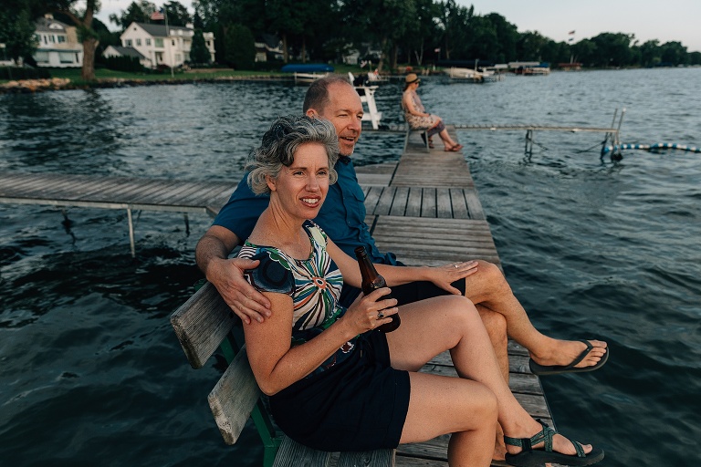 two adults share a beer on a pier overlooking the lake at sunset 