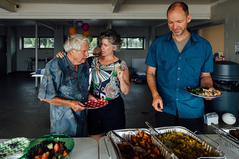 adult woman hugs elderly father in front of a buffet line at an event photography session