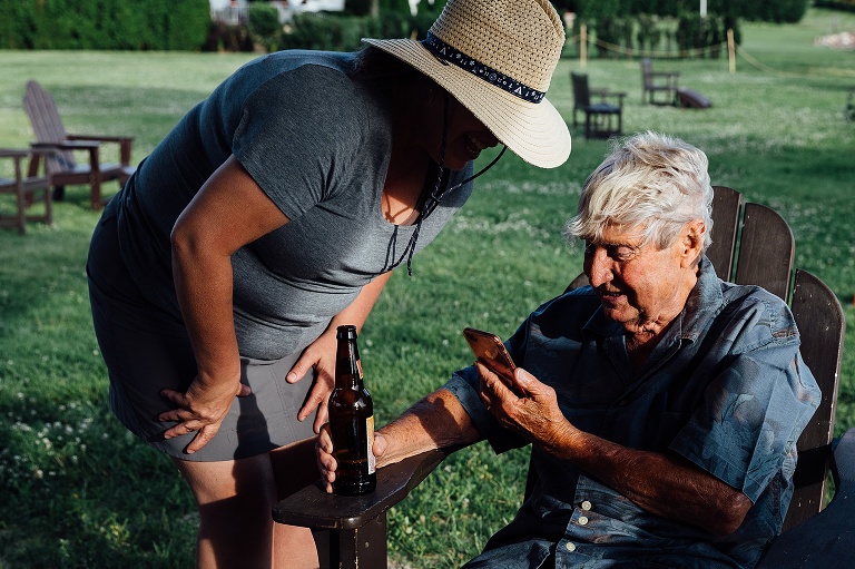 woman leans over elderly father and look at a cellphone together
