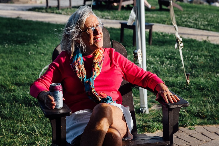 elderly woman sits in the sun listening to others at an event photography session
