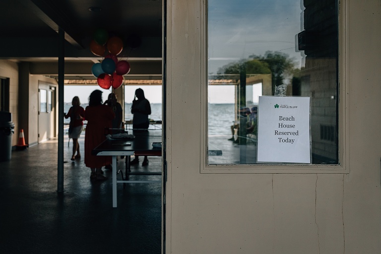 sign that reads 'beach house reserved today' hangs in window with balloons and people in the background for an event photography session