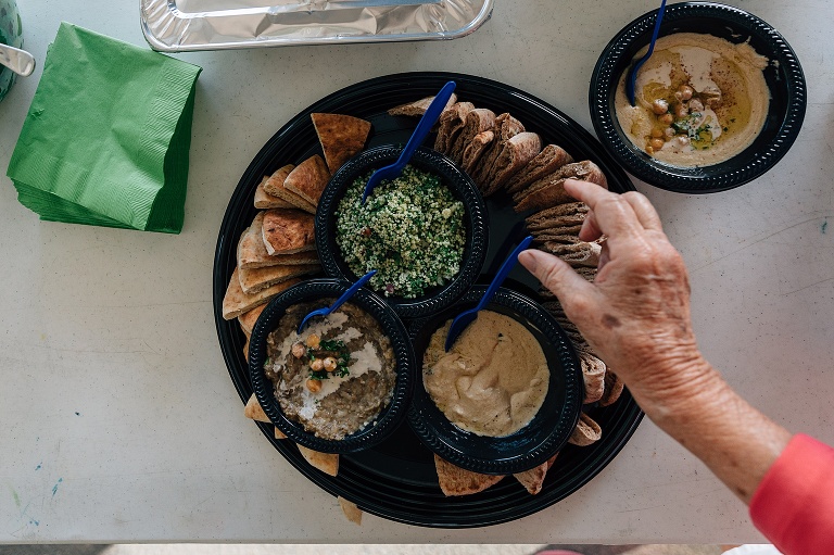 woman's hand approaches tray of pita, hummus, and dips at an event photography session