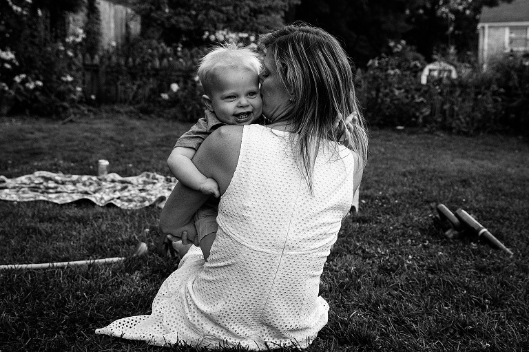 black and white. woman hugs smiling infant in the backyard on a summer night 