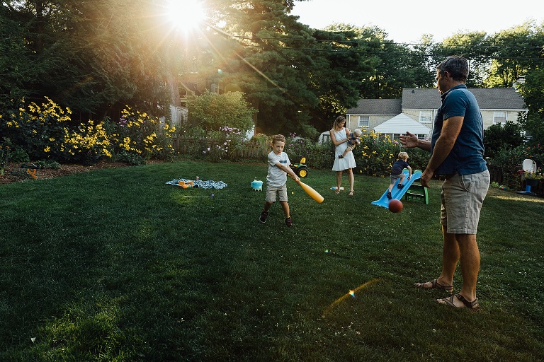 Family of five play baseball and climb toy slides in the backyard on a summer nights