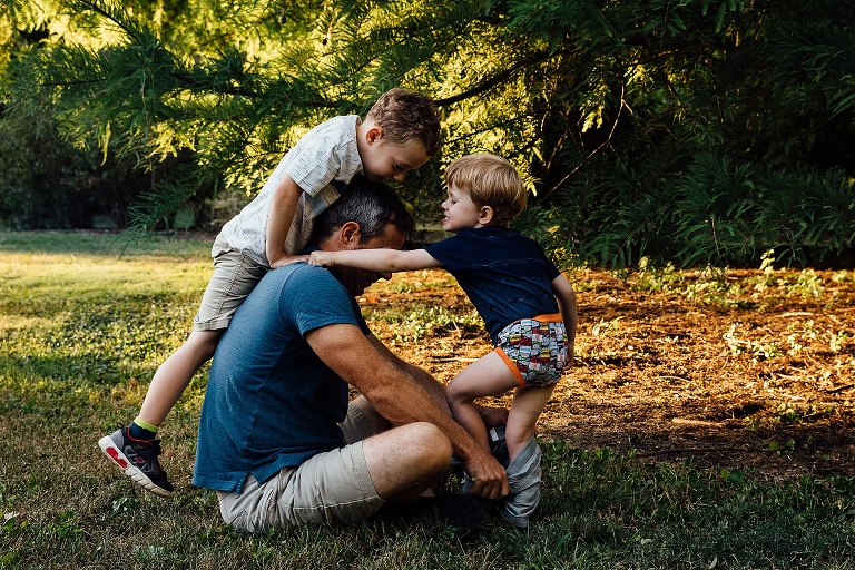 two boy climb on their dad as he tries to help one of them put his shorts on