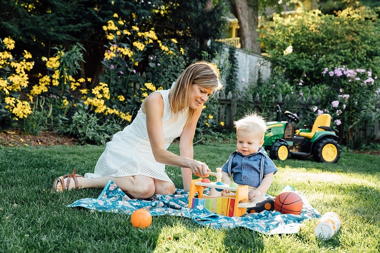 woman sits on a blanket in the backyard with infant son, playing a game. Backyard Summer Nights