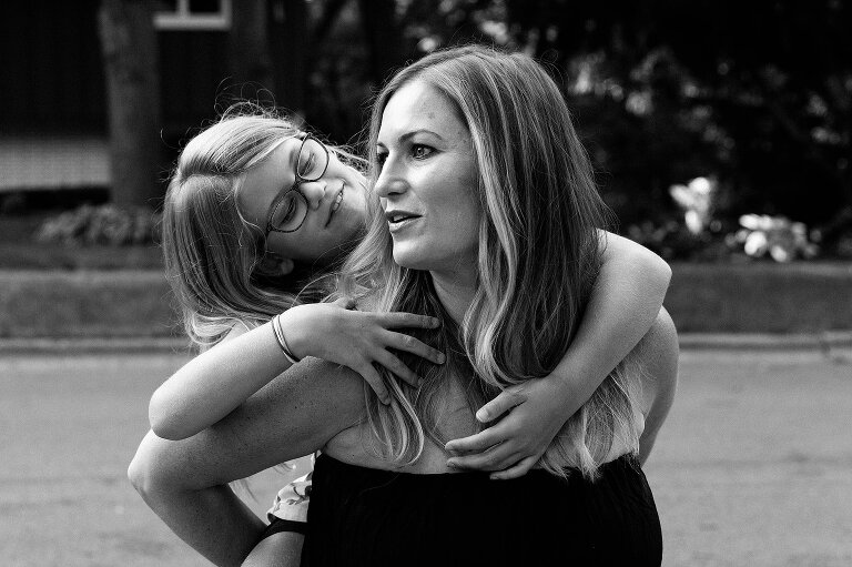mom holds daughter on her back and girl smiles sweetly at mother