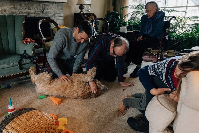 Two adults give a dog belly rubs in the middle of the living room floor