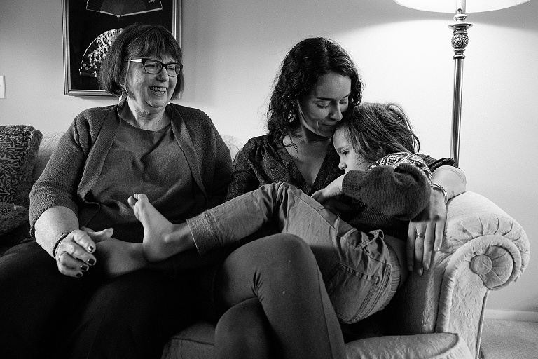 one woman embraces boy sitting on her lap while grandmother looks on. Black and white. 