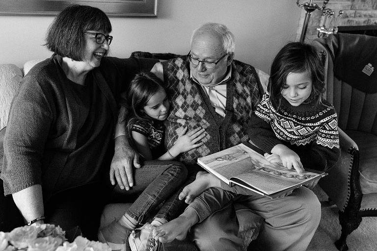 Grandparents sit and read with two grandchildren on a couch. Black and white. 