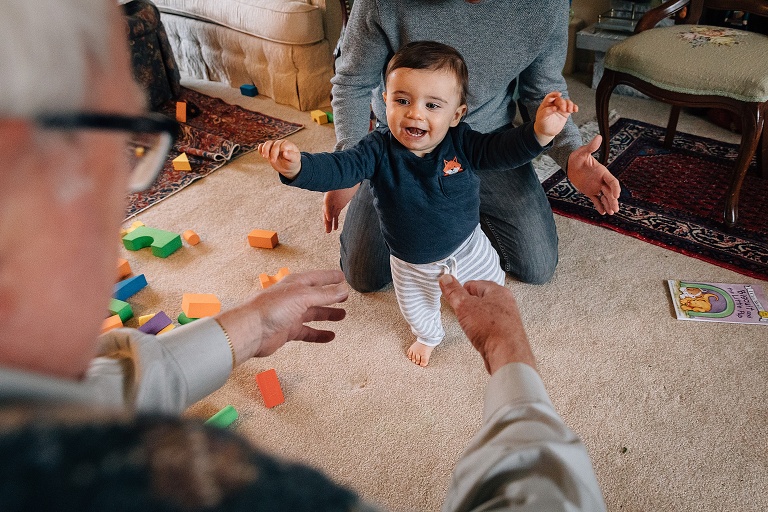 Toddler boy learns to walk and smiles as he falls into his grandfather's arms 