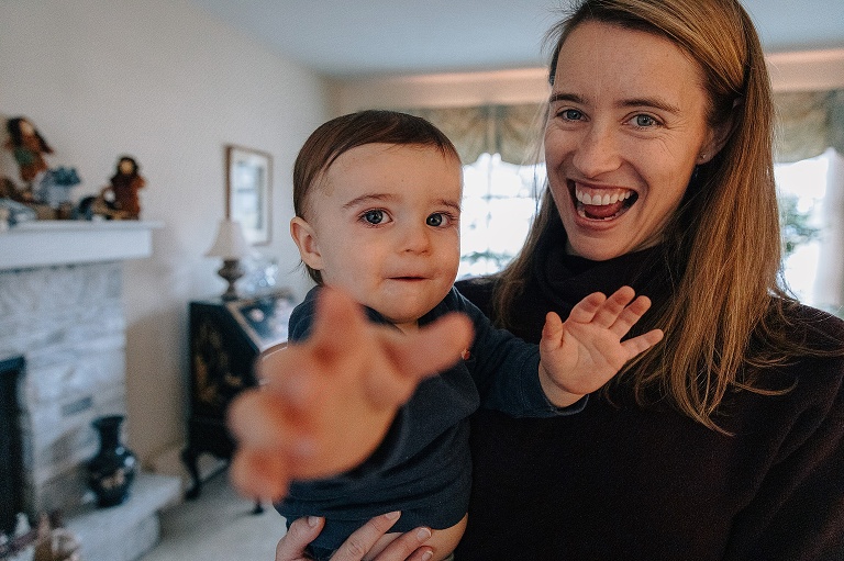 Mom and infant smile and baby reaches toward camera.